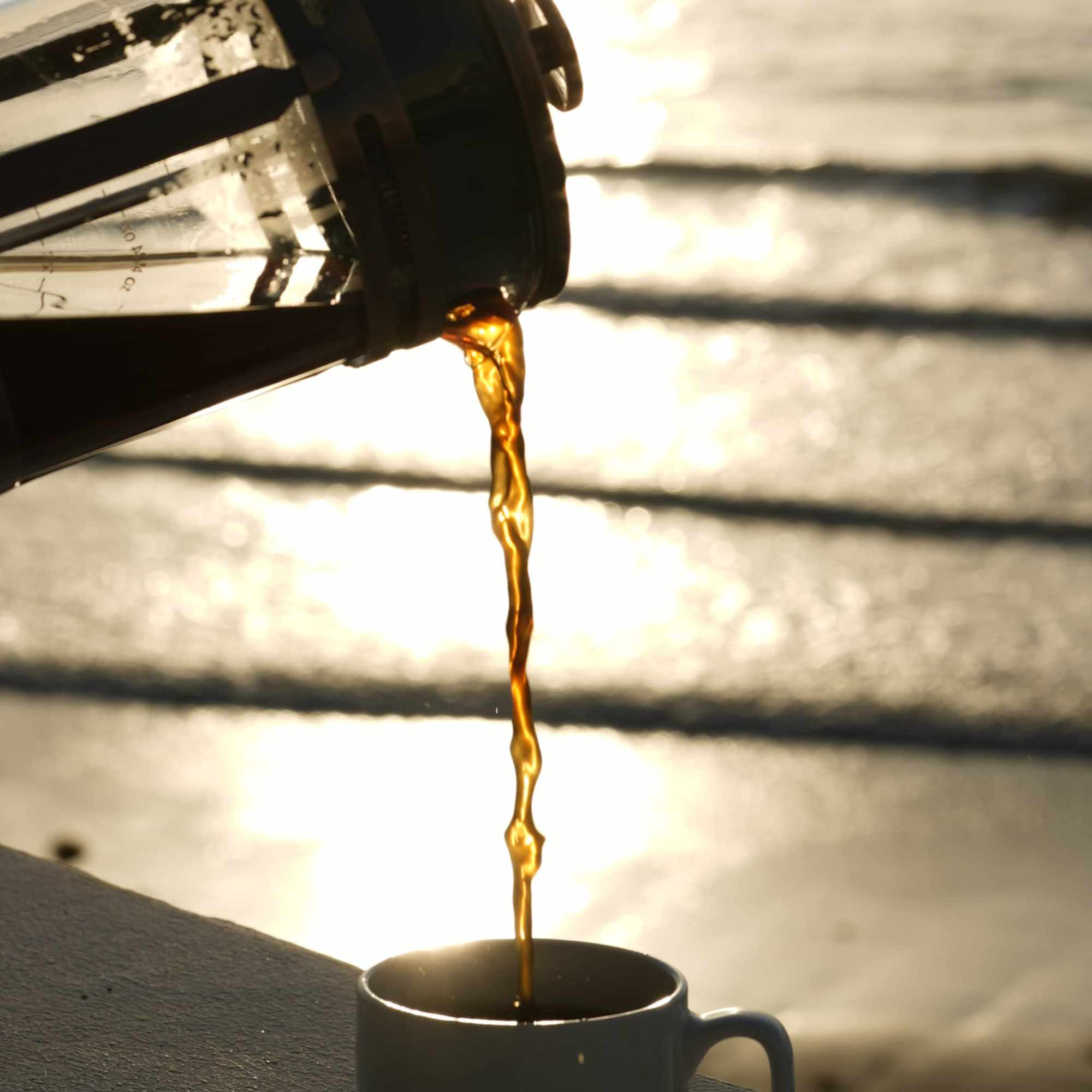 Chorro de café dorado cayendo de la prensa francesa a contraluz del atardecer